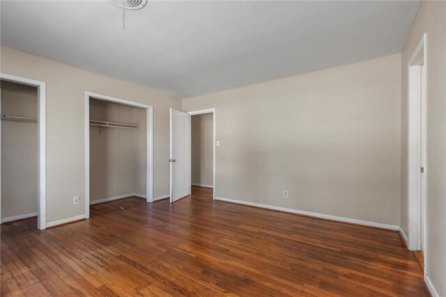 unfurnished bedroom with dark hardwood / wood-style flooring and two closets