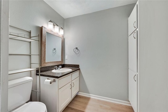 half bath with vanity, wood finished floors, toilet, and baseboards