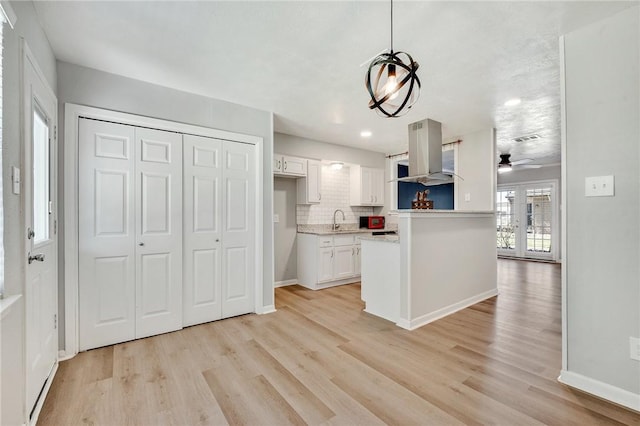 kitchen with island range hood, a sink, white cabinetry, light wood finished floors, and tasteful backsplash