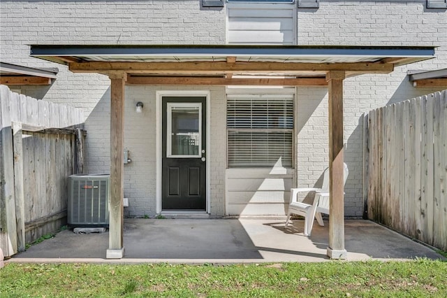 property entrance featuring brick siding, fence, and central air condition unit