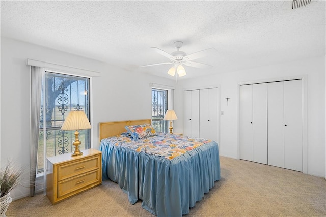 bedroom featuring visible vents, two closets, light colored carpet, a textured ceiling, and a ceiling fan