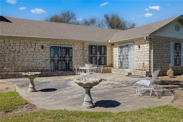 rear view of property featuring a patio area, stone siding, and roof with shingles