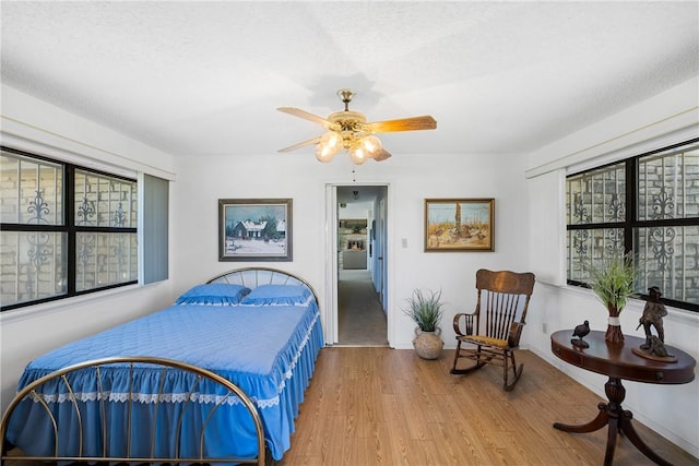 bedroom featuring multiple windows, a textured ceiling, wood finished floors, and a ceiling fan