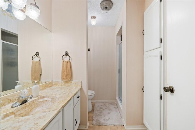 bathroom with vanity, baseboards, an enclosed shower, a textured ceiling, and toilet