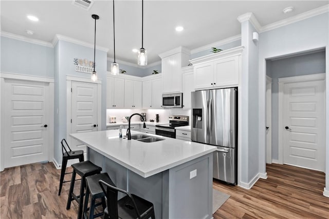 kitchen featuring visible vents, a sink, baseboards, stainless steel appliances, and an island with sink