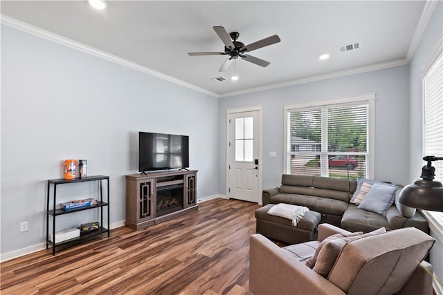 living area featuring visible vents, crown molding, wood finished floors, baseboards, and a ceiling fan