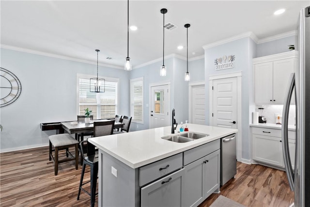 kitchen with crown molding, appliances with stainless steel finishes, a sink, dark wood-style floors, and an island with sink