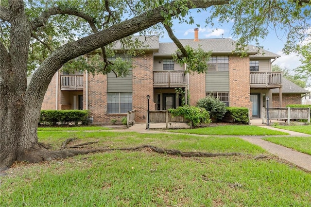 view of front of house with brick siding, a front lawn, and a balcony