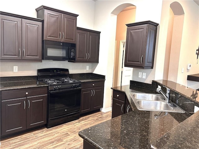 kitchen with dark brown cabinetry, light wood finished floors, arched walkways, black appliances, and a sink