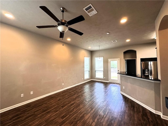 unfurnished living room featuring dark wood-style floors, arched walkways, visible vents, and baseboards