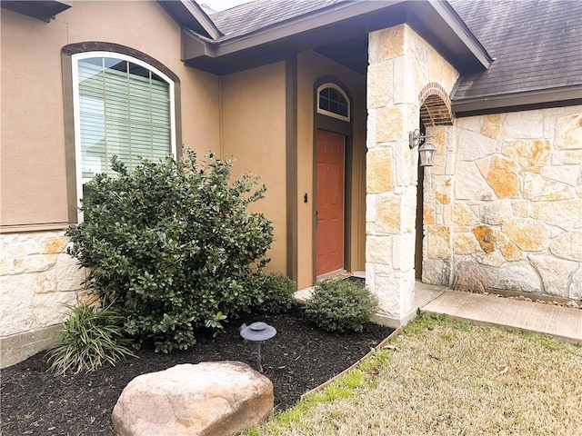 view of exterior entry featuring a shingled roof, stone siding, and stucco siding