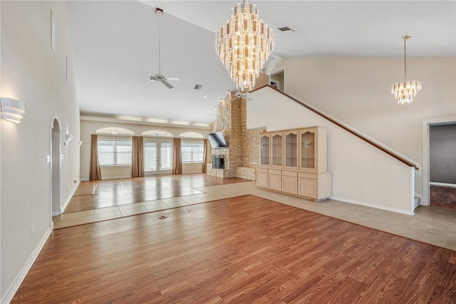 unfurnished living room featuring ceiling fan with notable chandelier, a towering ceiling, a fireplace, and hardwood / wood-style floors