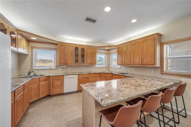 kitchen with sink, dishwasher, light stone counters, a kitchen bar, and kitchen peninsula