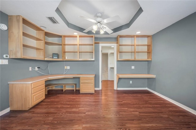 unfurnished office with dark hardwood / wood-style floors, ceiling fan, a tray ceiling, and built in desk