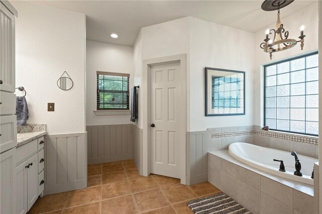 full bathroom with tile patterned flooring, wainscoting, vanity, a notable chandelier, and a garden tub