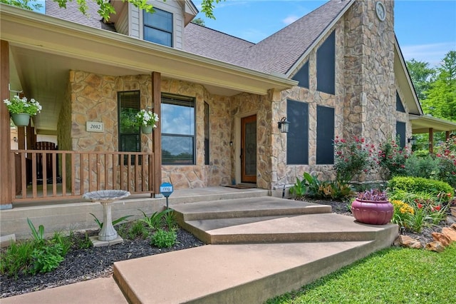 view of exterior entry with a porch, stone siding, and roof with shingles
