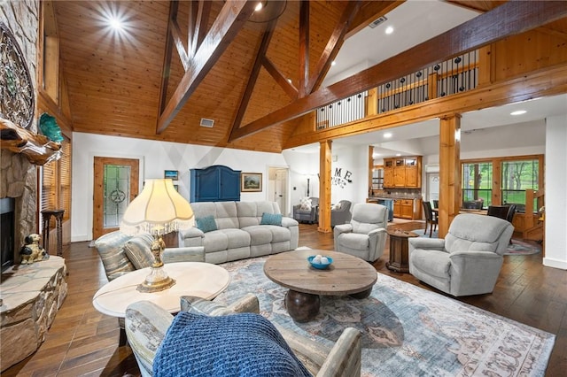 living room with visible vents, hardwood / wood-style floors, beamed ceiling, a stone fireplace, and high vaulted ceiling