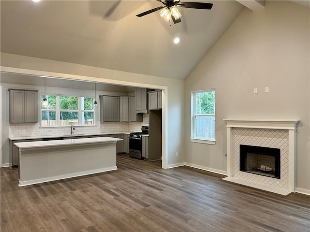 kitchen with gray cabinetry, stainless steel range, ceiling fan, a kitchen island, and a tiled fireplace