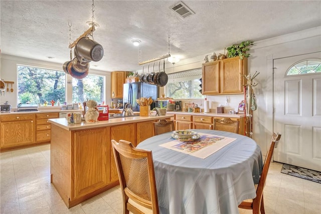 kitchen featuring stainless steel refrigerator, a center island, crown molding, a textured ceiling, and light tile patterned flooring