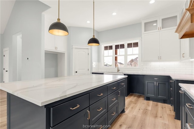 kitchen featuring a center island, hanging light fixtures, light wood-type flooring, tasteful backsplash, and white cabinetry