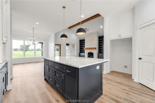 kitchen with light stone countertops, white cabinets, hanging light fixtures, and a kitchen island