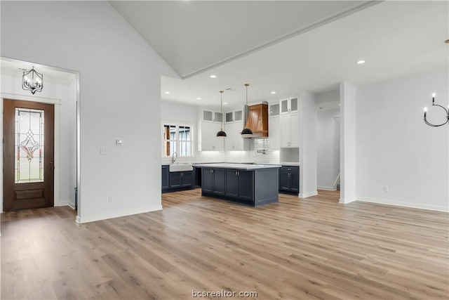 kitchen with premium range hood, white cabinets, sink, hanging light fixtures, and light hardwood / wood-style floors