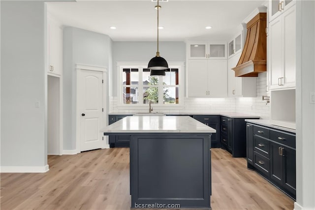 kitchen with custom exhaust hood, white cabinets, hanging light fixtures, a kitchen island, and light hardwood / wood-style floors