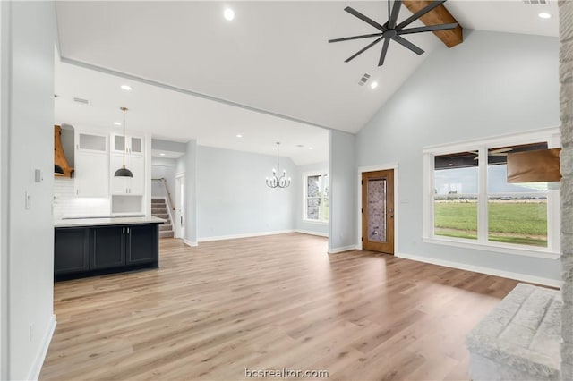 unfurnished living room with beam ceiling, ceiling fan with notable chandelier, high vaulted ceiling, and light hardwood / wood-style flooring