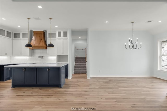 kitchen with white cabinetry, tasteful backsplash, light hardwood / wood-style flooring, pendant lighting, and custom range hood