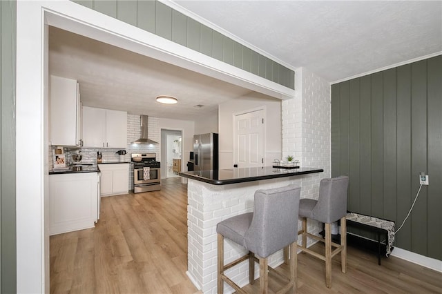 750 Garden Acres Blvd, Bryan, TX 77802 - kitchen featuring appliances with stainless steel finishes, wall chimney range hood, dark countertops, decorative backsplash, and light wood-style floors