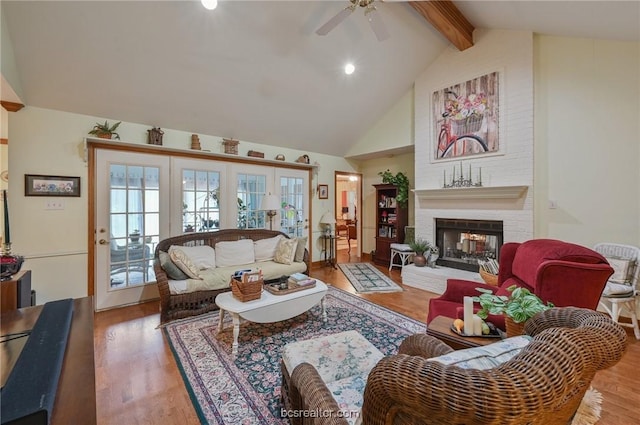 living room featuring vaulted ceiling with beams, ceiling fan, wood-type flooring, and a brick fireplace