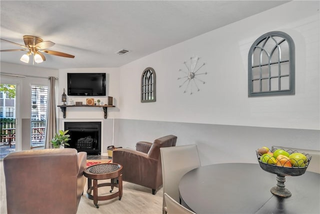 living area with a fireplace with flush hearth, a ceiling fan, visible vents, and wood finished floors