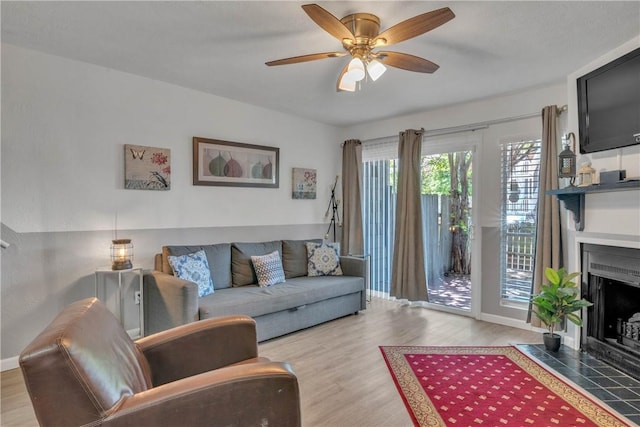 living area featuring a fireplace with flush hearth, wood finished floors, baseboards, and ceiling fan