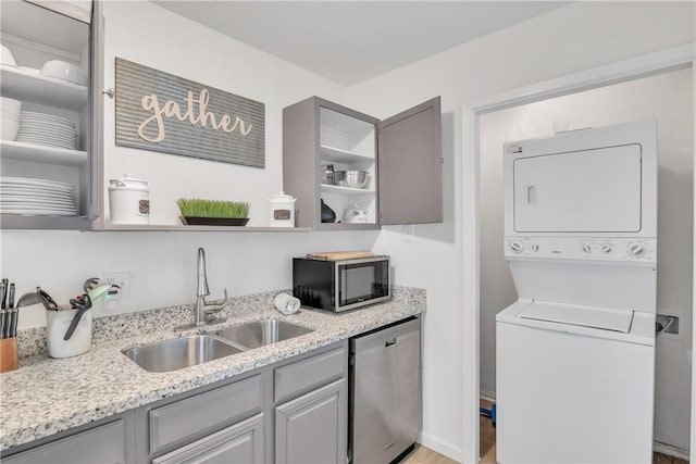 kitchen with stainless steel appliances, gray cabinetry, and stacked washer / dryer