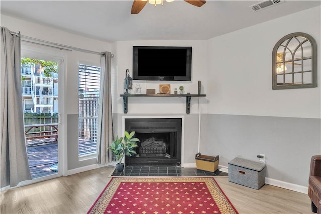 living area with a fireplace with flush hearth, wood finished floors, visible vents, and ceiling fan
