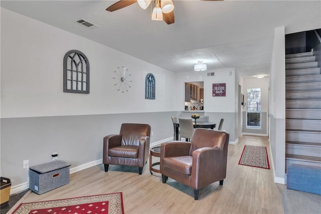 sitting room featuring a ceiling fan, stairs, light wood-style flooring, baseboards, and visible vents