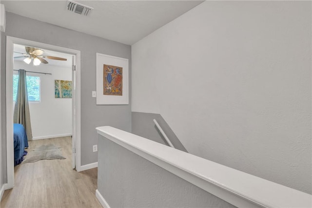 corridor with baseboards, light wood finished floors, an upstairs landing, and visible vents