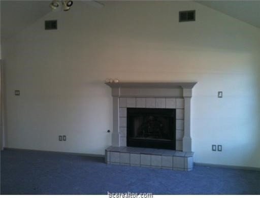 unfurnished living room with a fireplace, dark colored carpet, and high vaulted ceiling