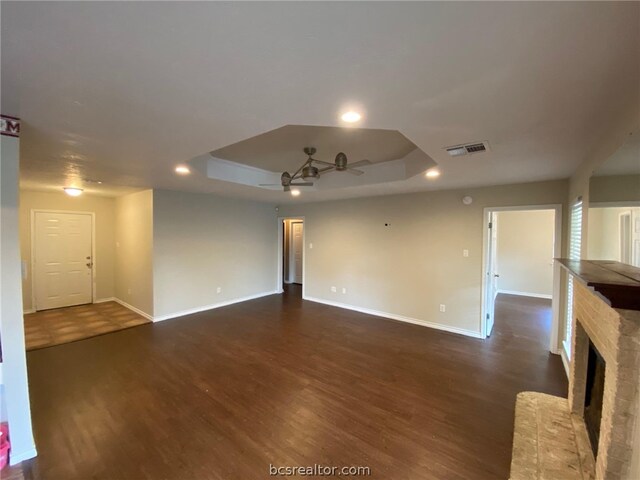 unfurnished living room with a raised ceiling, ceiling fan, dark hardwood / wood-style flooring, and a fireplace