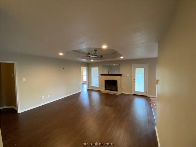 unfurnished living room with a raised ceiling, plenty of natural light, dark wood-type flooring, and ceiling fan