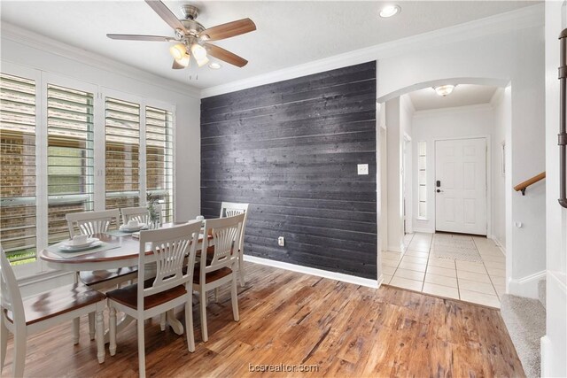 dining area featuring ceiling fan, wood-type flooring, crown molding, and wooden walls