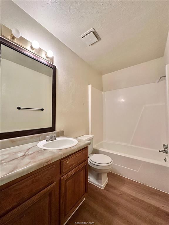 full bathroom featuring vanity, toilet, a textured ceiling, wood-type flooring, and tub / shower combination