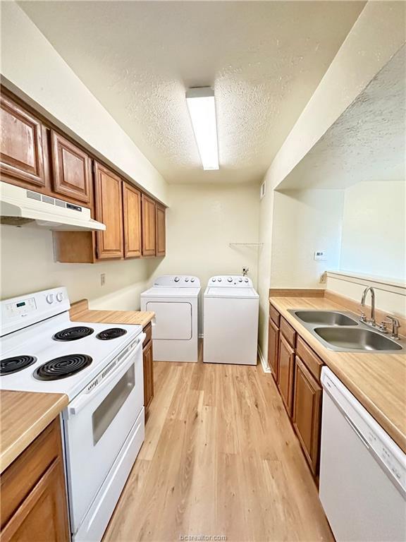 kitchen featuring white appliances, a textured ceiling, sink, independent washer and dryer, and light hardwood / wood-style floors