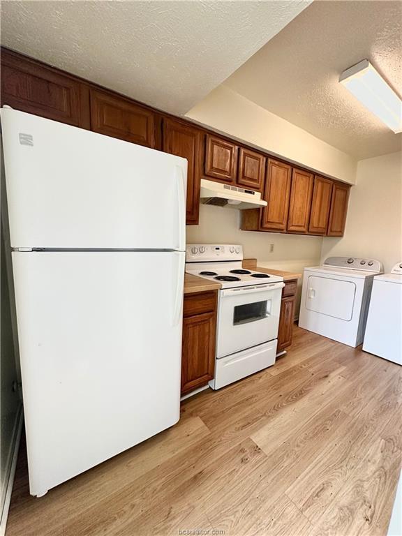 kitchen with light hardwood / wood-style floors, white appliances, a textured ceiling, and separate washer and dryer