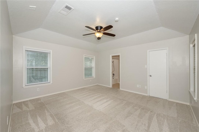 empty room with light colored carpet, a tray ceiling, visible vents, and baseboards