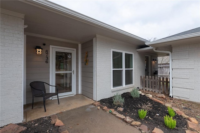 view of exterior entry featuring brick siding and fence