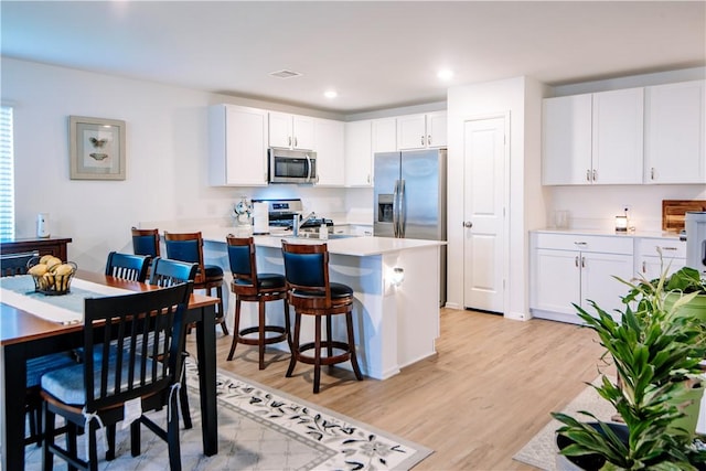 kitchen featuring light wood finished floors, stainless steel appliances, a kitchen bar, light countertops, and white cabinets