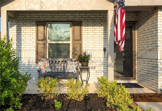 view of exterior entry featuring covered porch and brick siding