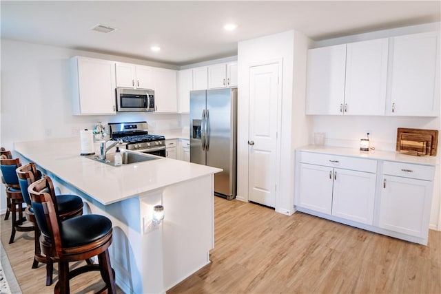 kitchen with a breakfast bar area, white cabinets, a sink, stainless steel appliances, and light wood-type flooring