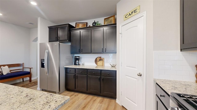 kitchen with appliances with stainless steel finishes, light stone countertops, decorative backsplash, and light wood-type flooring